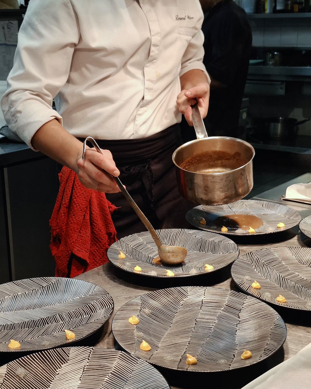 Un chef nappe une série d’assiettes à la louche, en cuisine