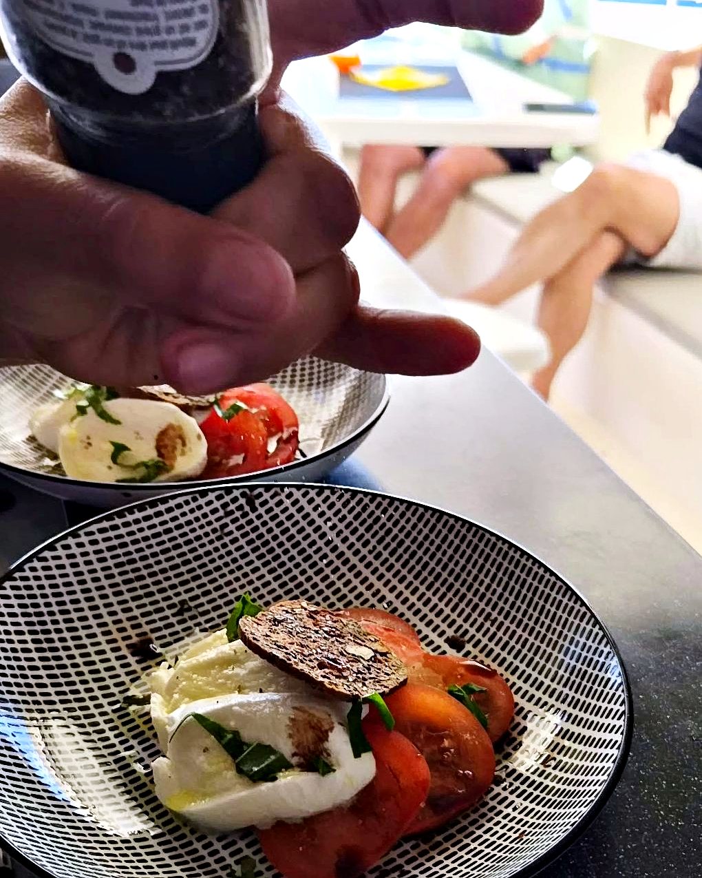 Le chef poivre les assiettes, le carré du catamaran et la mer derrière