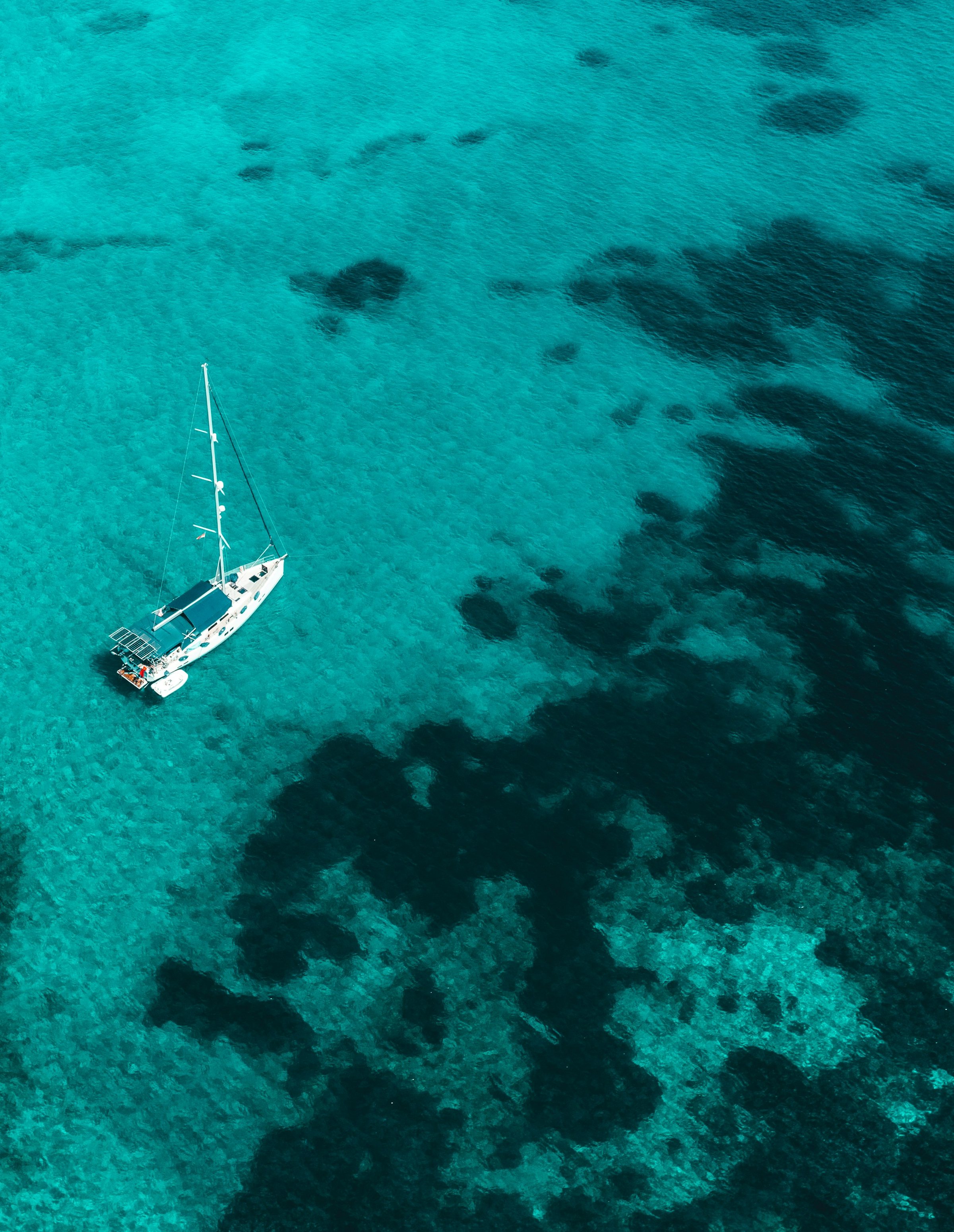 Un voilier au mouillage sur une eau turquoise, vu du ciel
